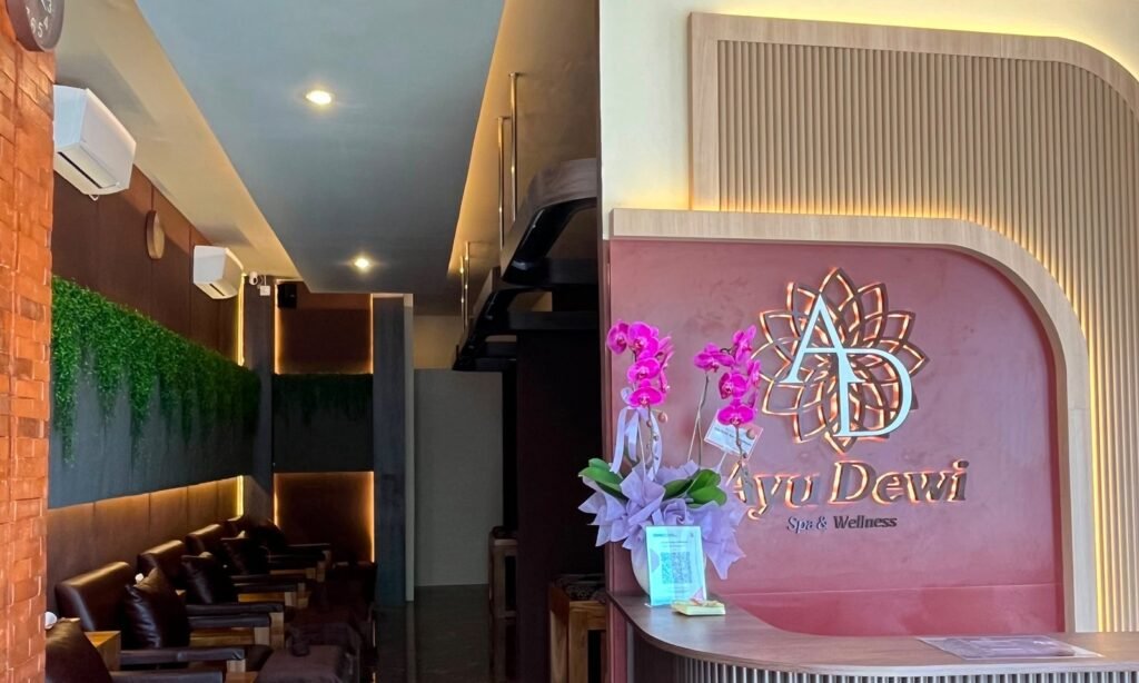 The Ayu Dewi Spa reception counter and backlit logo, with the reflexology lounge beyond