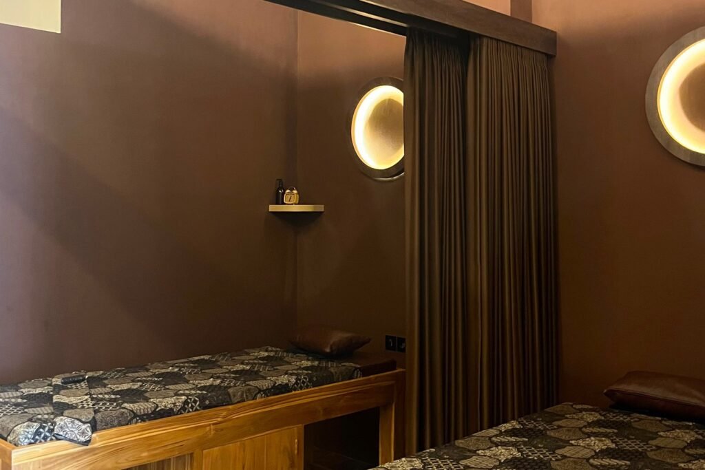 Two teak massage beds with batik covers and warm round wall lights in a private treatment room